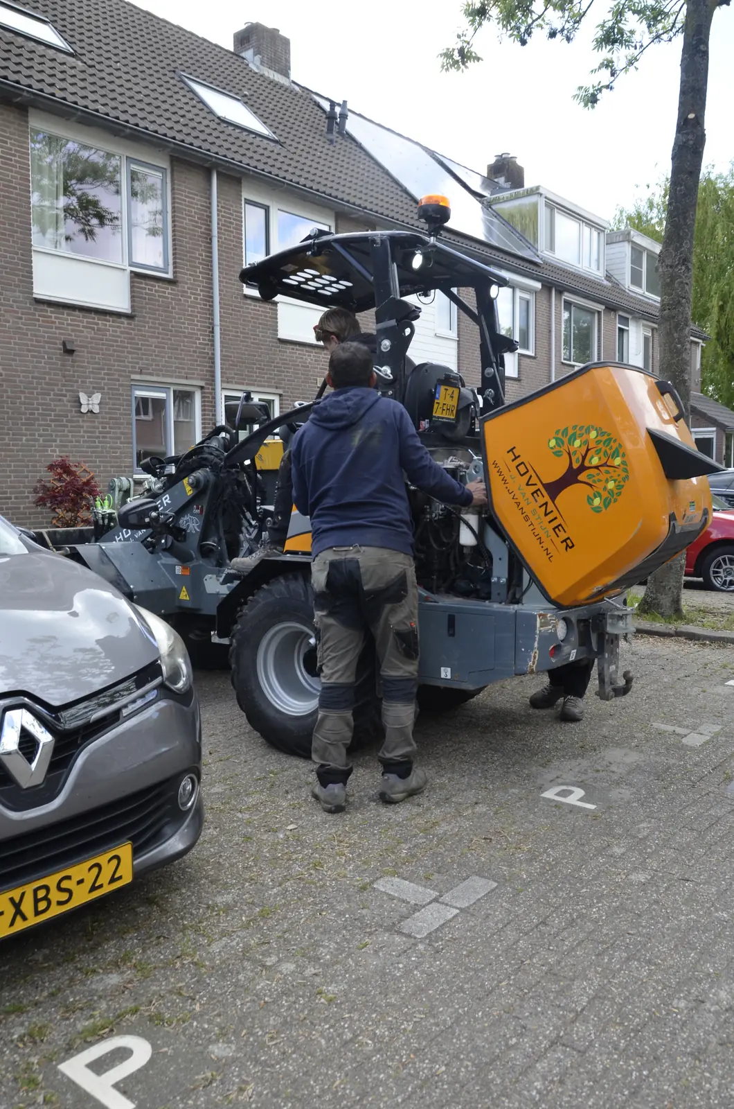 Hovenier laadt de minidumper met ons logo van de aanhanger op straat