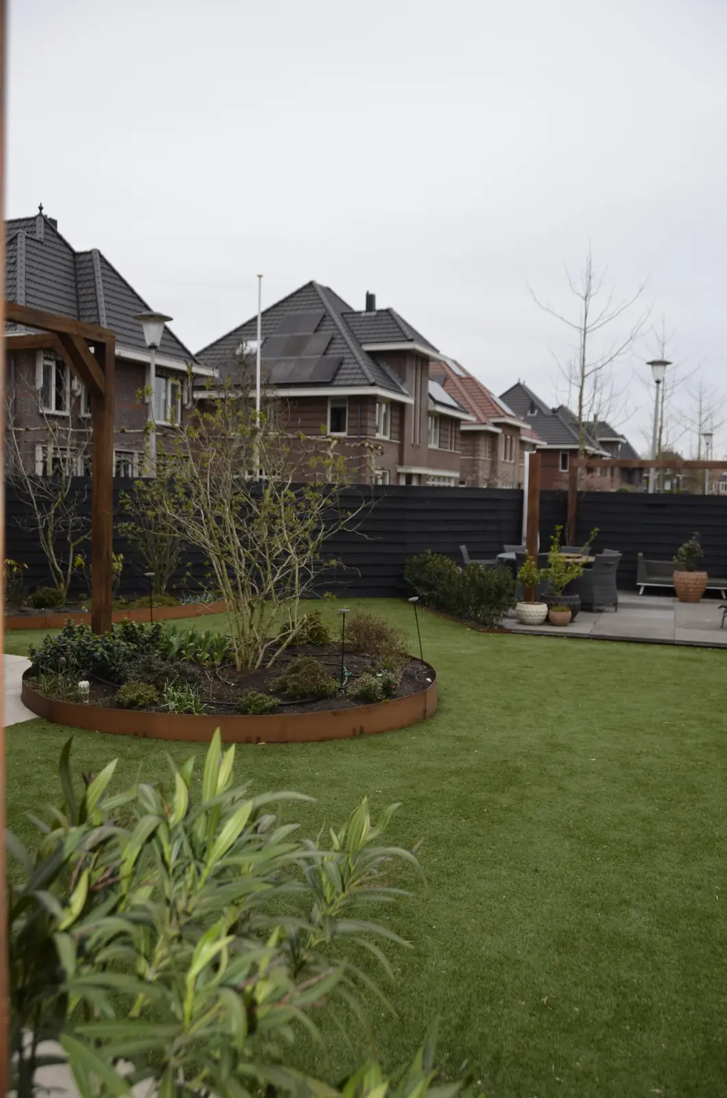 Overzicht van de achtertuin met de ronde cortenstalen border midden in het gazon