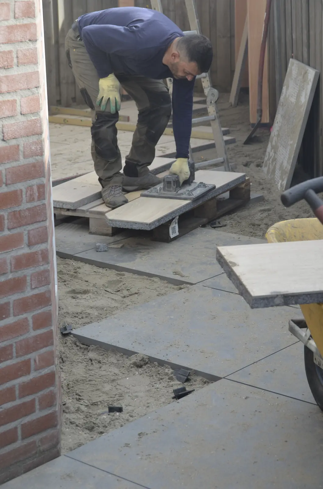 Hovenier legt een tegel op het zandbed langs de gevel
