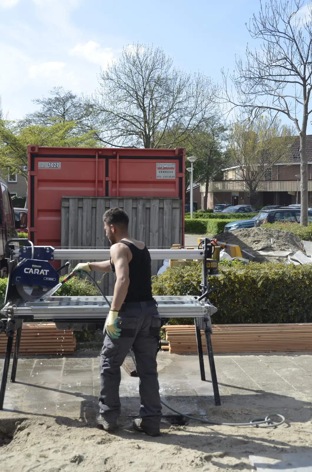 Hovenier zaagt materiaal op maat naast de container