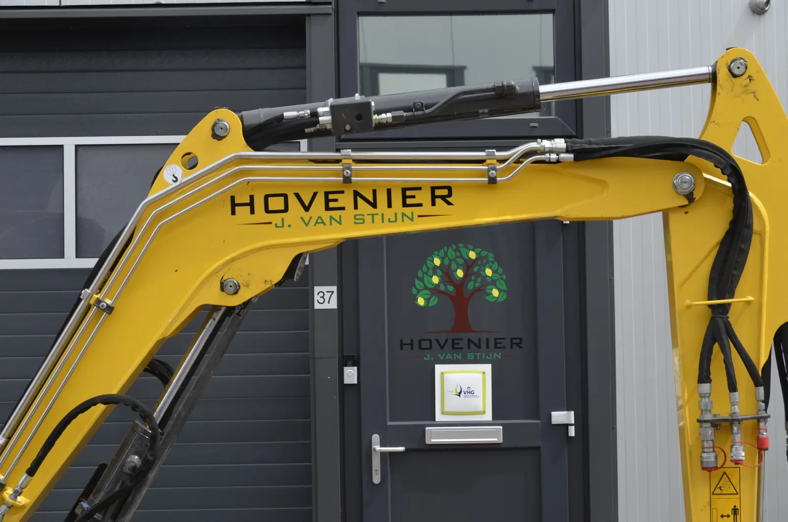 De giek van onze New Holland graafmachine met onze naam erop, voor het bedrijfspand