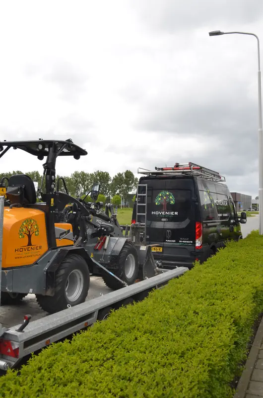 Onze shovel rijdt de kipper op, achter de bedrijfsbus