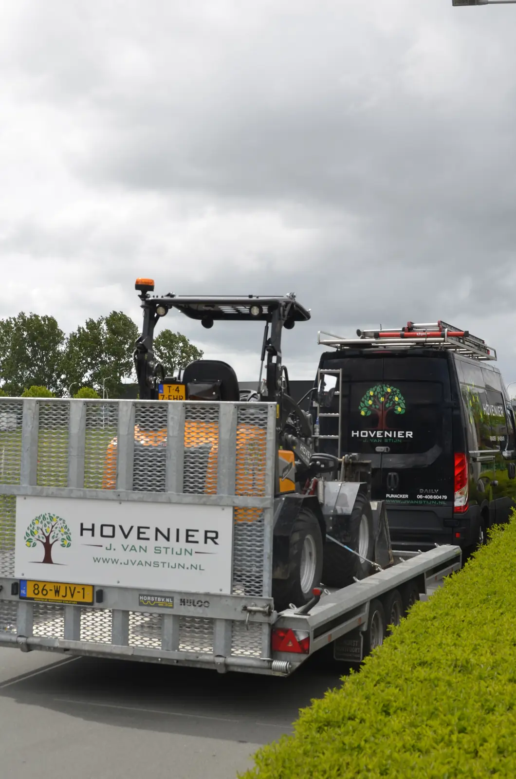 De shovel op de aanhanger achter de bus, onderweg naar een klus