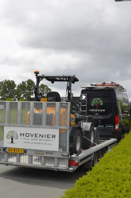 De shovel op de aanhanger achter de bus, onderweg naar een klus