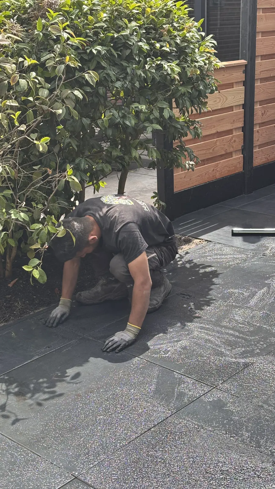 Hovenier legt op de knieën tegels langs de beplanting