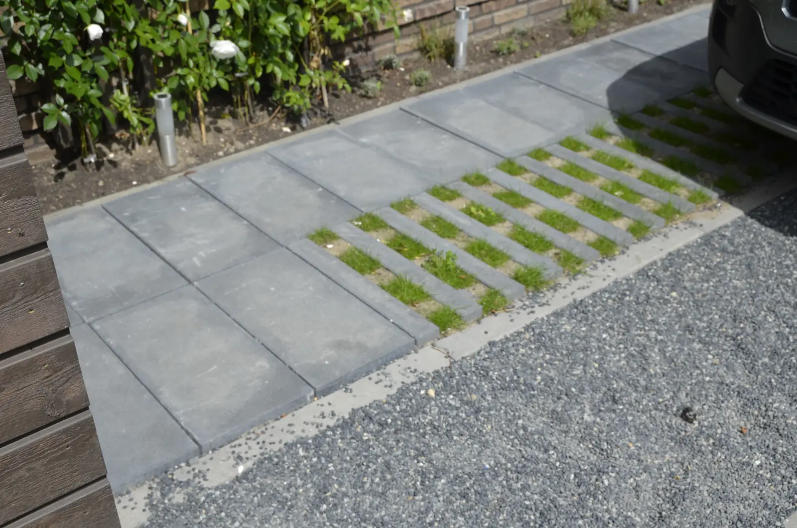 Terras van grote zandkleurige keramische tegels met eettafel en stapstenen in het gras